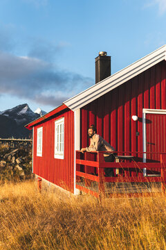 Happy man leaning on railing at porch of log cabin