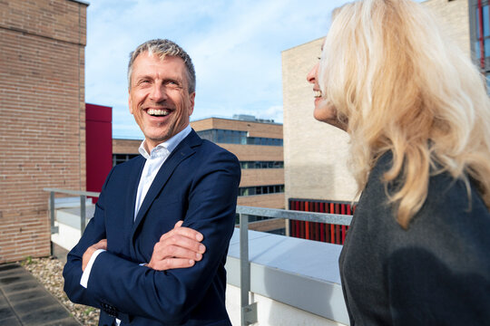 Happy businessman with arms crossed standing next to colleague on terrace