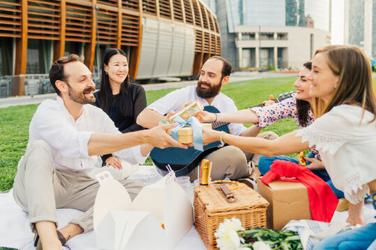 Happy women giving gifts to man and enjoying picnic in park