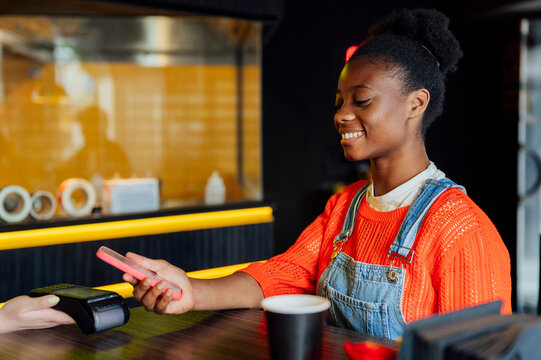Happy young woman paying through smart phone at restaurant