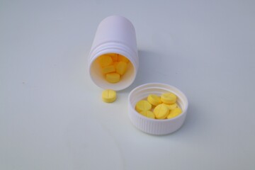 Yellow colored medicine tablets or vitamin C medication spilling from the bottle in close up view on white background.