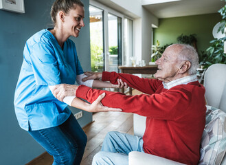 Happy nurse helping senior man and teaching exercise at home