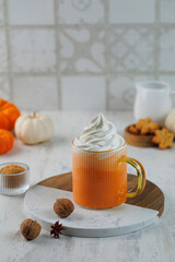 A glass of autumn pumpkin latte with whipped cream and spices. Coffee with pumpkin and cinnamon on light grey background. Vertical