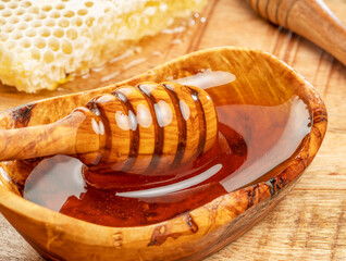 Natural organic honey in wooden bowl, honey dipper and honeycombs are near.