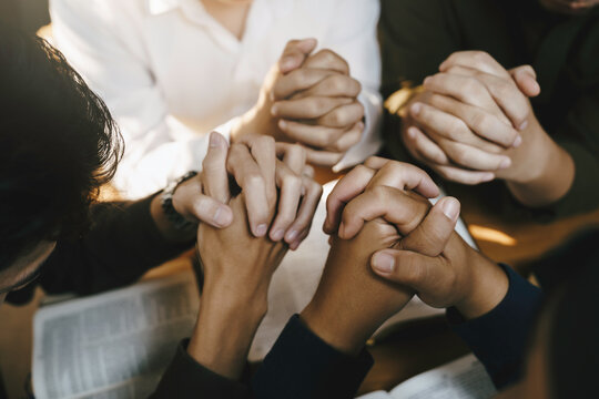 Christian and prayer. Christian group of people holding hands praying worships together to believe and Bible on a wooden table for devotional for prayer meeting concept. - Powered by Adobe