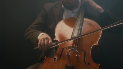 Cropped shot of handsome male cellist in suit sitting on chair while playing cello on black background