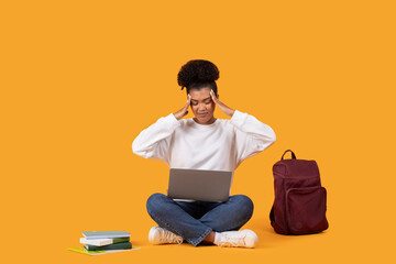 A young woman with dark hair sits on a yellow background, looking stressed. She is holding her head...