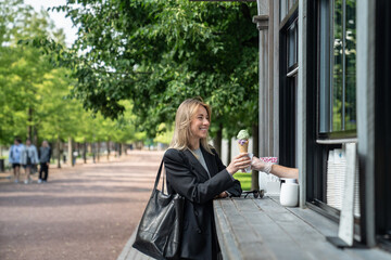 Contented woman buy ice cream in outdoor stand cafe, smiling takes waffle cone from window of stall...