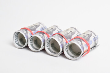 A row of rolled hundred dollar bills with rubber bands isolated on white background, stack of one hundred dollars American cash money bills rolled up with rubber band.