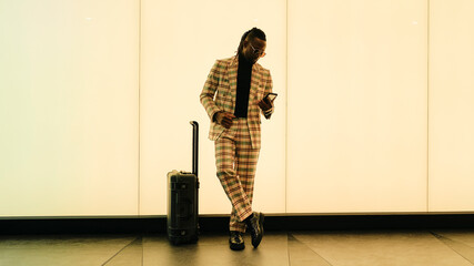 Businessman using smart phone standing by luggage near illuminated wall