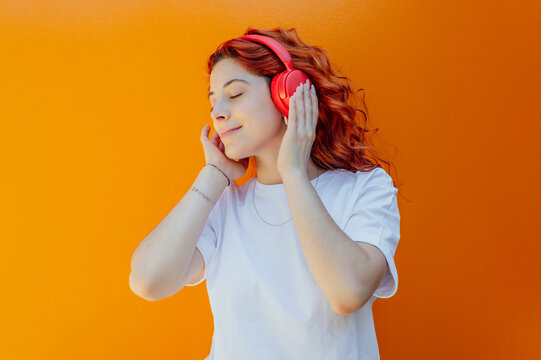 Young woman listening to music through wireless headphones against colored background