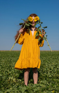 Teenage girl with red hair in a yellow dress holding sunflowers in a green field