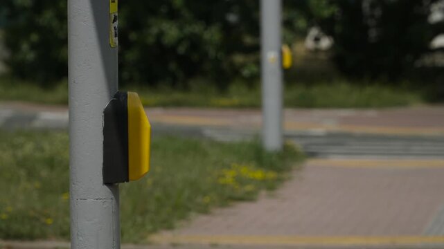 Side view of yellow touch sensor on pole near a pedestrian crossing, no people. Cars drive quickly along road past the equipment to call green traffic light for pedestrian.