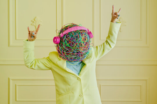 Woman with mask of chaotic thoughts making horn sign in front of wall