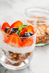 Gourmet breakfast: berry parfait of strawberries, blueberries and granola with delicate Greek yogurt, mascarpone and whipped cream on a gray background. Selected focus. vertical photo