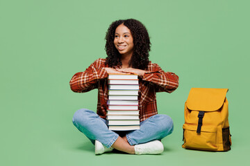 Full body young teen girl student wear brown yellow casual clothes backpack bag sits hold pile of books look aside on area isolated on plain green background. High school university college concept.