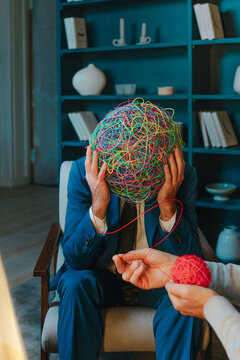 Patient with head in hands sitting with psychotherapist holding wire ball