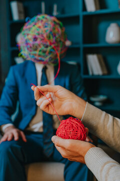 Psychotherapist's hand untangling wire from patient's mask of chaos