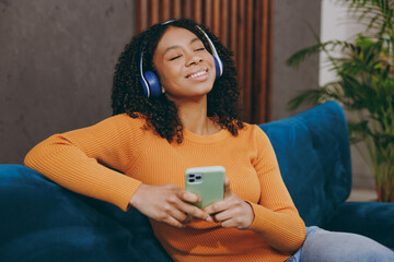 Little fun kid teen girl wear casual clothes headphones listen music use mobile cell phone sit on...