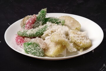 A white plate filled with sweet Indonesian treats, Lupis and Cenil, served with grated coconut.