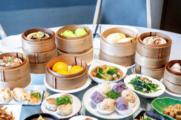 Image of various Chinese dim sum in a bamboo steamer, equipped with chopsticks and tea, on a wooden table. 
