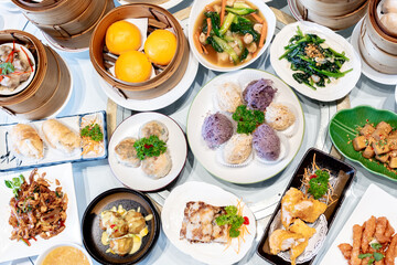 Image of various Chinese dim sum in a bamboo steamer, equipped with chopsticks and tea, on a wooden table. 