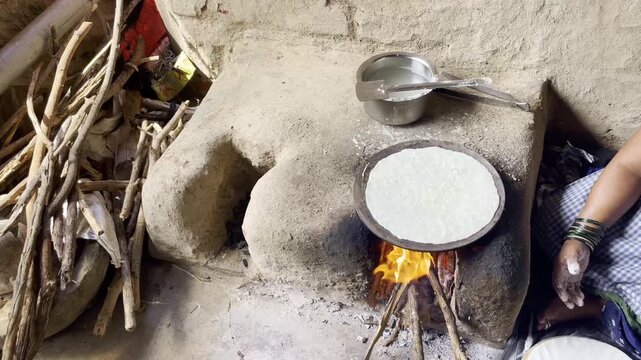 Indian woman cooking traditional indian bread, bhakri using firewood in-earthen chulhas Maharashtra India 4K