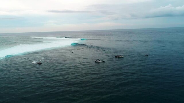 Drone orbits above support boats and surfer lineup crowd at Cloudbreak Fiji