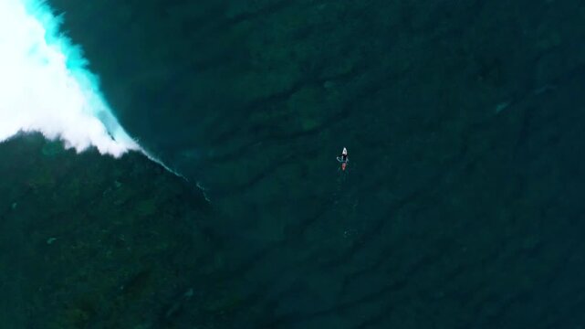 Drone top down orbits above surfer paddling in ocean at Cloudbreak Fiji