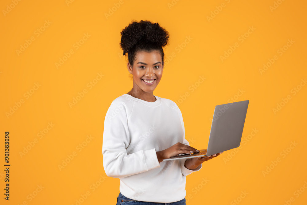 Poster a young woman with a bright smile uses a laptop while standing in front of a yellow background. she 