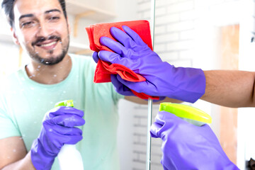 Handsome man cleaning mirror in the bathroom