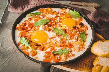 Scrambled eggs with tomatoes, peppers, shallots and bacon in a cast iron skillet with slices of...