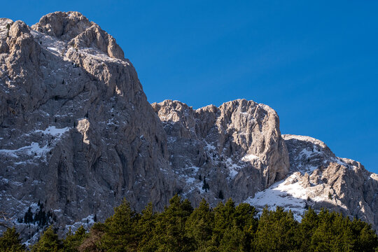 A closer look at a rugged mountain peak partially covered with snow and bordered by dense pine trees under a clear blue sky, capturing the essence of raw natural beauty in Pedraforca in Catalonia
