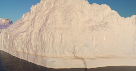 Close up panorama frozen glacier in polar ocean. Massive ice wall under bright sunset light and blue sky. Large iceberg towering icy polar water. Antarctica travel exploration. Cinematic ecology scene