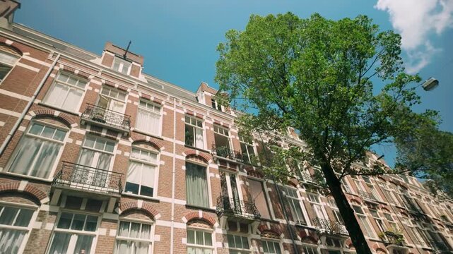 Low angle POV footage showcasing Amsterdam school architecture and residential houses in the heart of the city center. The elegant facades and tree-lined streets highlight the city's historic charm.
