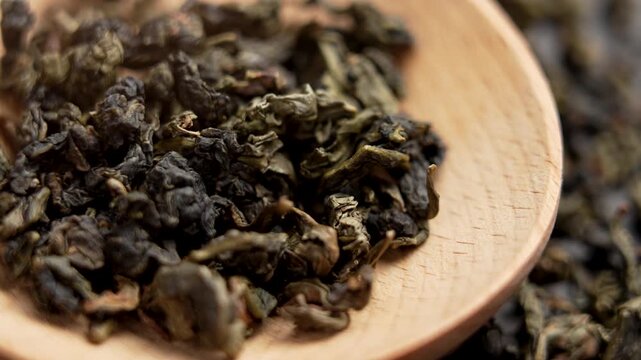 Chinese Oolong tea hand-harvested in the lush mountains of Taiwan. Green dried leaves in wooden spoon. Macro shot. Rotation