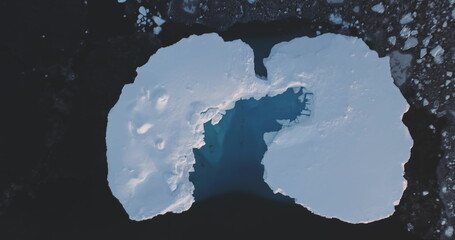 Melting cave in ice floe snow covered iceberg aerial top down view. Glacier float in polar frozen icy ocean. Ecology, melting ice, climate change global warming. Antarctica travel and exploration