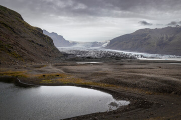 Small lake reflecting cloudy sky in front of glacier tongue in iceland