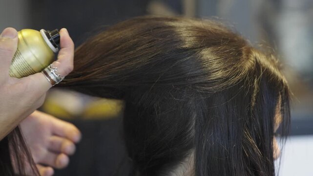 Coiffeur qui met de la laque sur les cheveux d'une femme brune. Hairdresser putting hairspray on a brunette woman's hair.