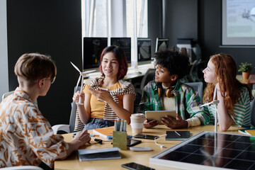 Multi-ethnic group of modern teenagers sitting at table in classroom discussing renewable energy...