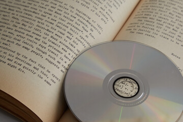 Compact disc against the background of an open book with text, foreign language learning, electronic library, analog information carriers; new vs old, digital vs analog, traditional vs modern