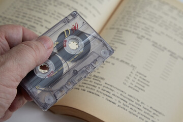 Hand holding an old audio cassette against the background of an old English textbook, old-fashioned...