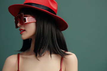 Woman, red hat, sunglasses, green background a stylish woman in a vibrant red hat and chic...