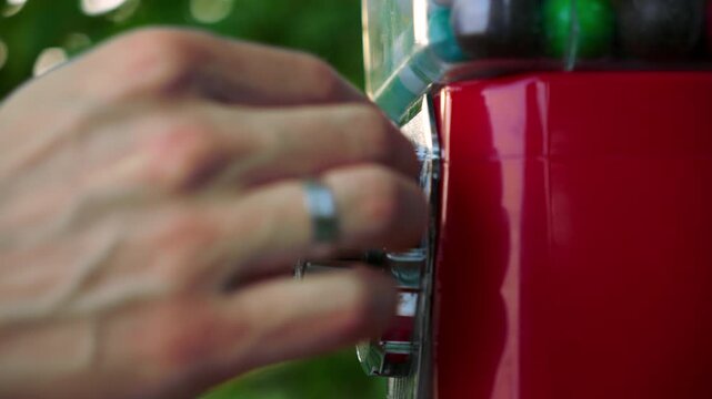 buying gum balls from a red machine installed outside in the park.