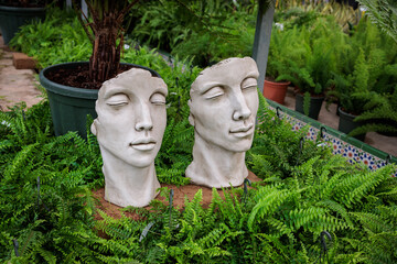 Two stone busts resting on ferns in garden center