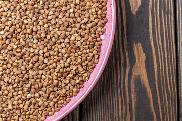 Buckwheat Grains on Plate on Wooden Background, Top View, Copy Space.Hulled kernels of buckwheat grains close up. Food background.