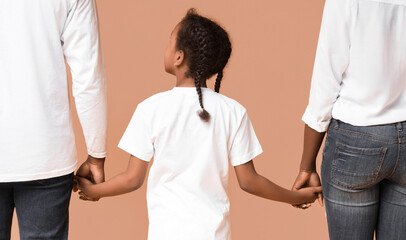 Obraz premium Family connection. Rear view of african mother, father and daughter holding hands together, yellow studio background, closeup