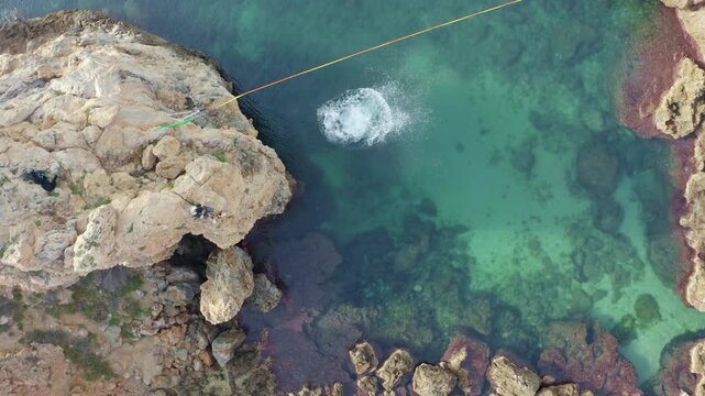 Aerial top shot of a man executing a perfect gainer off a 7m cliff into gorgeous turquoise water near a slackline close up