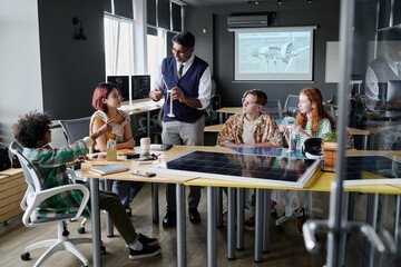 Wide shot of teacher showing wind turbine model to group of teen students during Environmental Education class