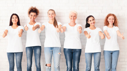 Fototapeta premium Breast Cancer. Group Of Mixed Ladies In Pink T-Shirts With Cancer Ribbons Gesturing Thumbs Up Standing On White Background. Panorama